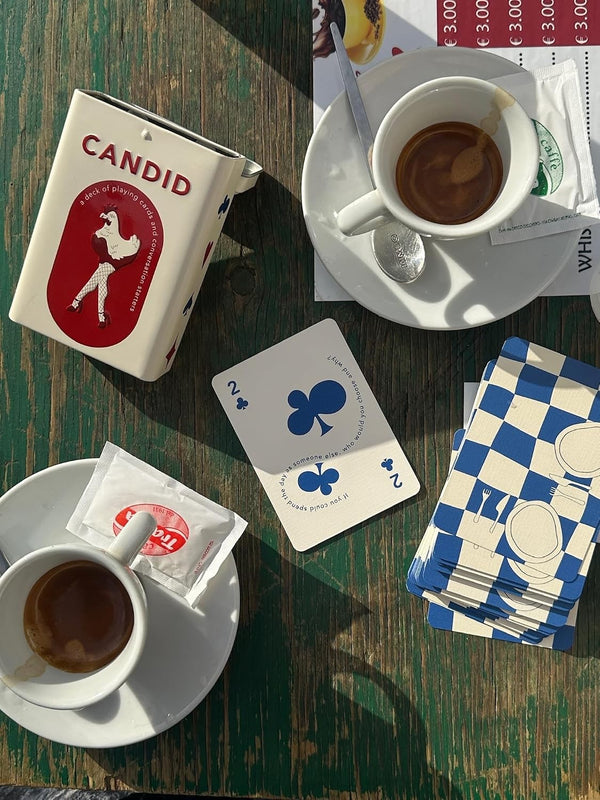 CANDID tin and cards on a green cafe table between two espressos